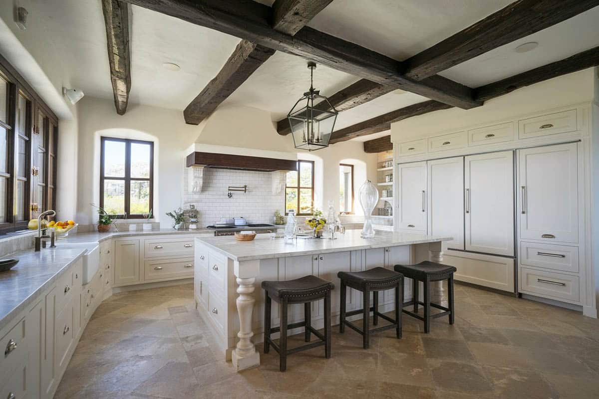 Kitchen with white cabinets, limestone floor and exposed beams on the ceiling