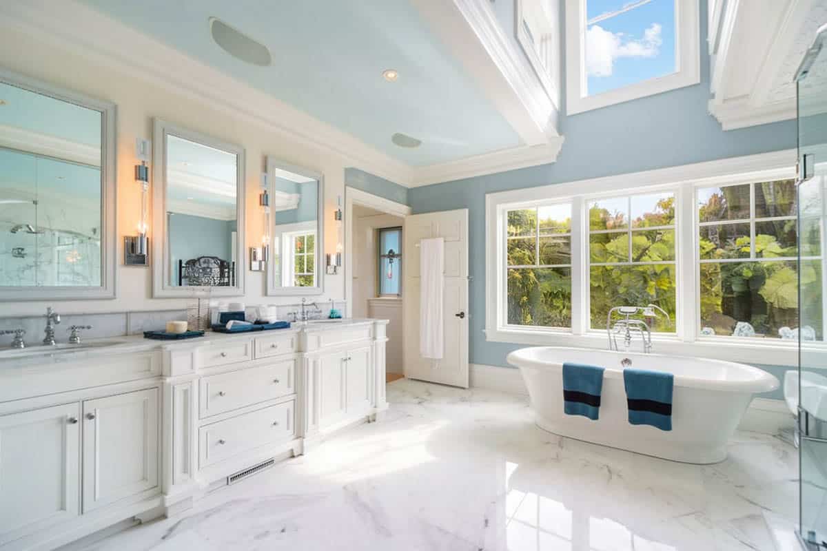 Bathroom with white vanity cabinets, blue walls and bathtub with picture windows
