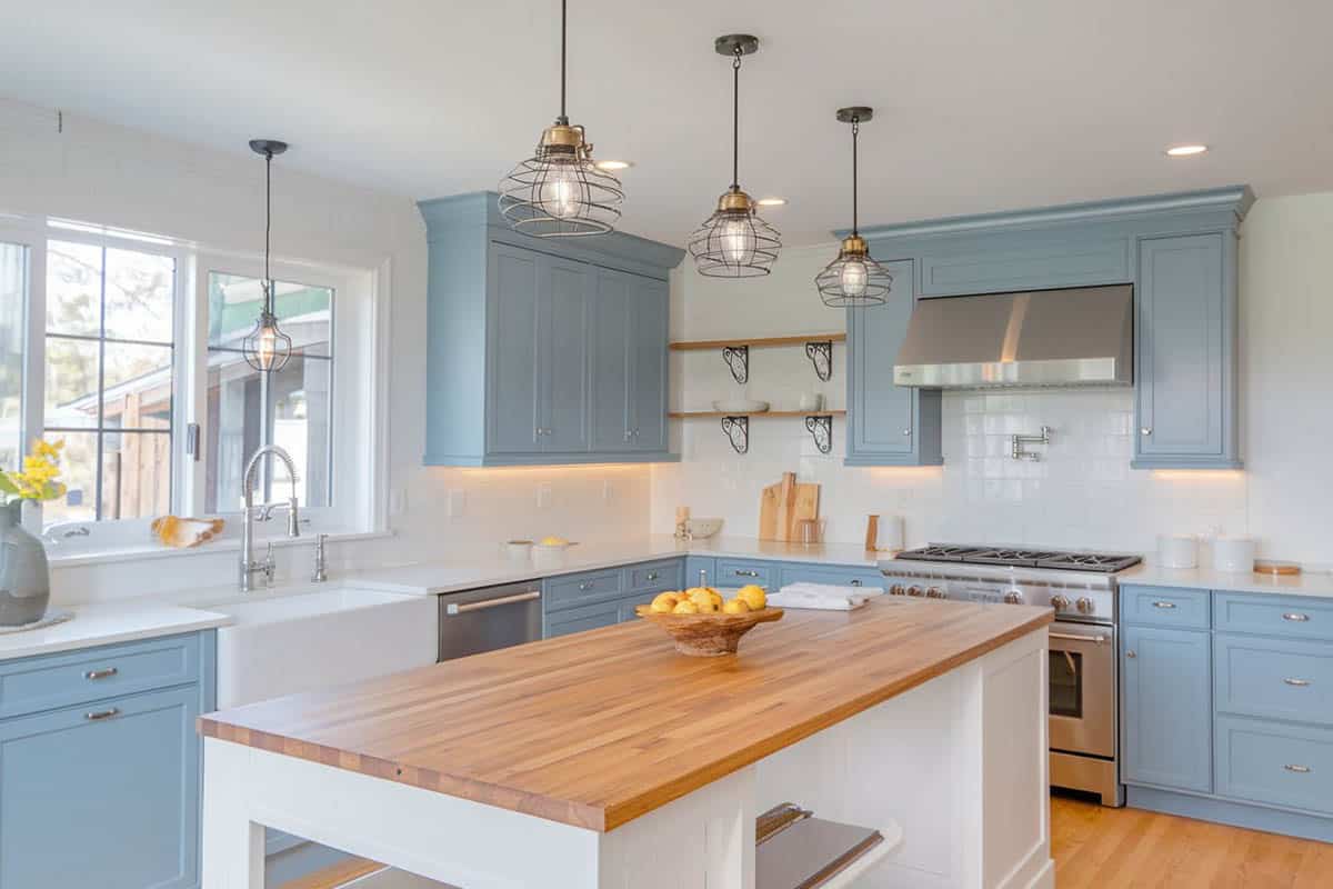 Farmhouse kitchen with light blue cabinets, single basin farmhouse sink, viking range and wood counter island painted white