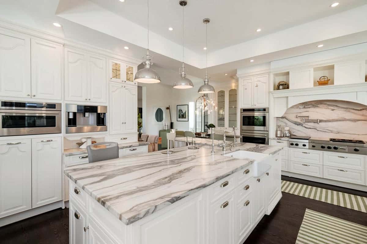 Luxury transitional style kitchen with white recessed panel cabinets, calacatta marble counter, espresso oak hardwood floors and metal pendant lights