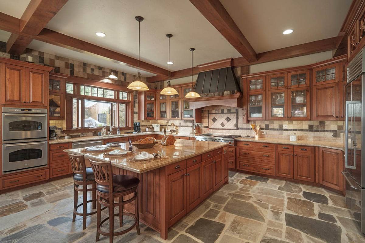 Kitchen with stone floors, wrought iron pendant lights and natural wood raised panel cabinets