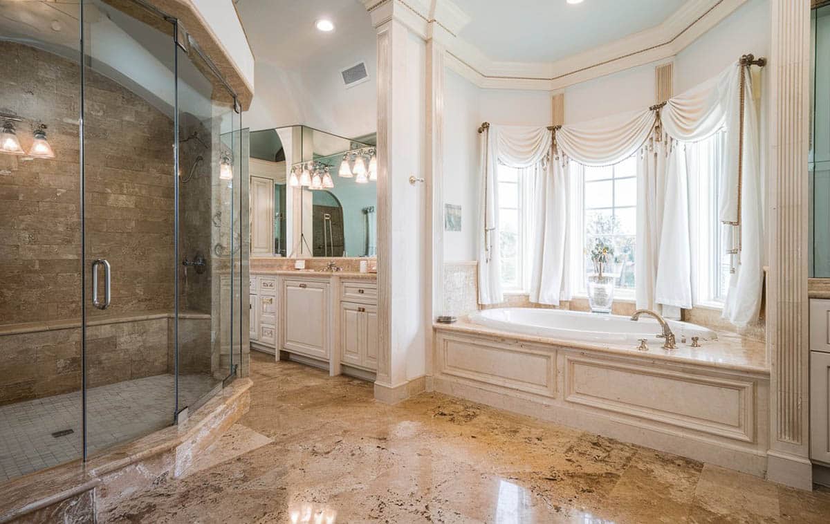 Traditional luxury bathroom with rough travertine enclosure and large enclosed tubs
