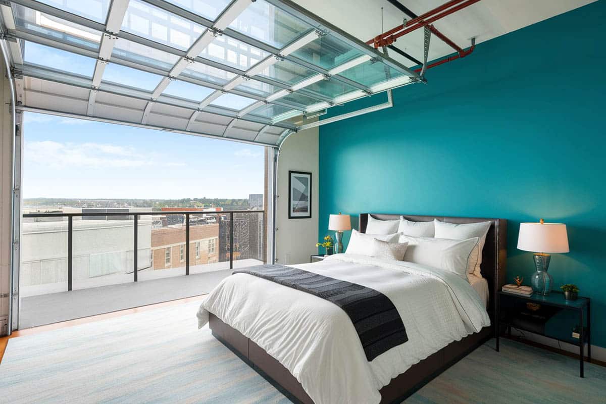 Bedroom with roll up door teal accent wall balcony and city views