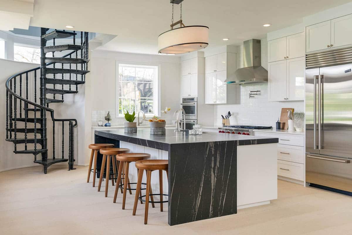 Waterfall island countertop in black marble, winding staircase and steel kitchen appliances
