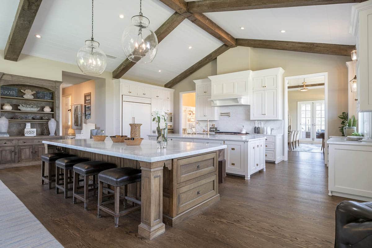 Large open concept kitchen with vaulted ceiling, exposed beams, white cabinets, wood flooring and contrasting islands