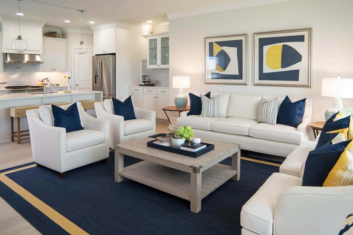 Open plan layout with dark blue rug, white sofa set, blue pillows and recessed lights