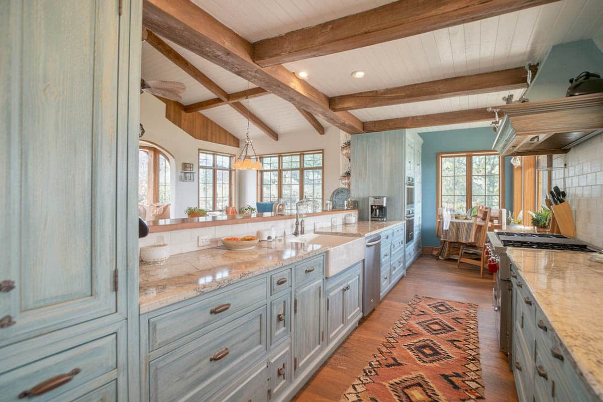 Kitchen with light green weathered cabinets, wood floors and exposed beams