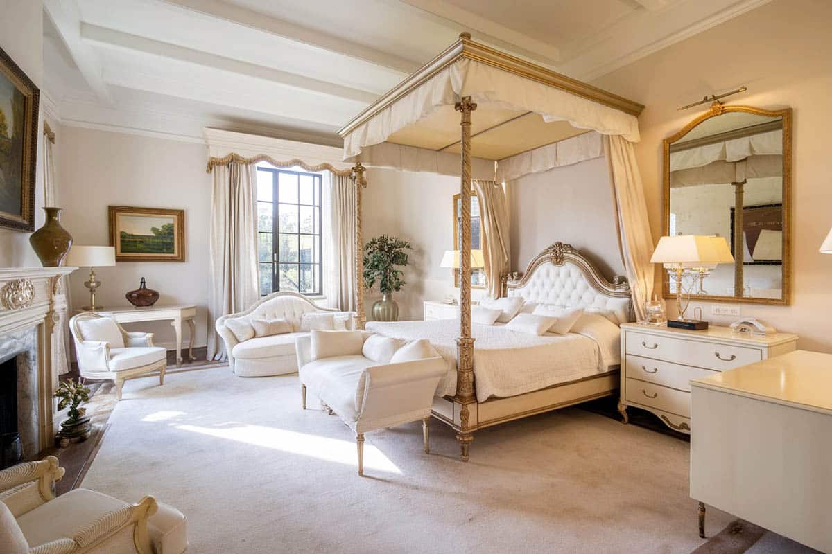 White theme french style bedroom with four poster bed, gilded gold mirror, and white bed bench and furniture
