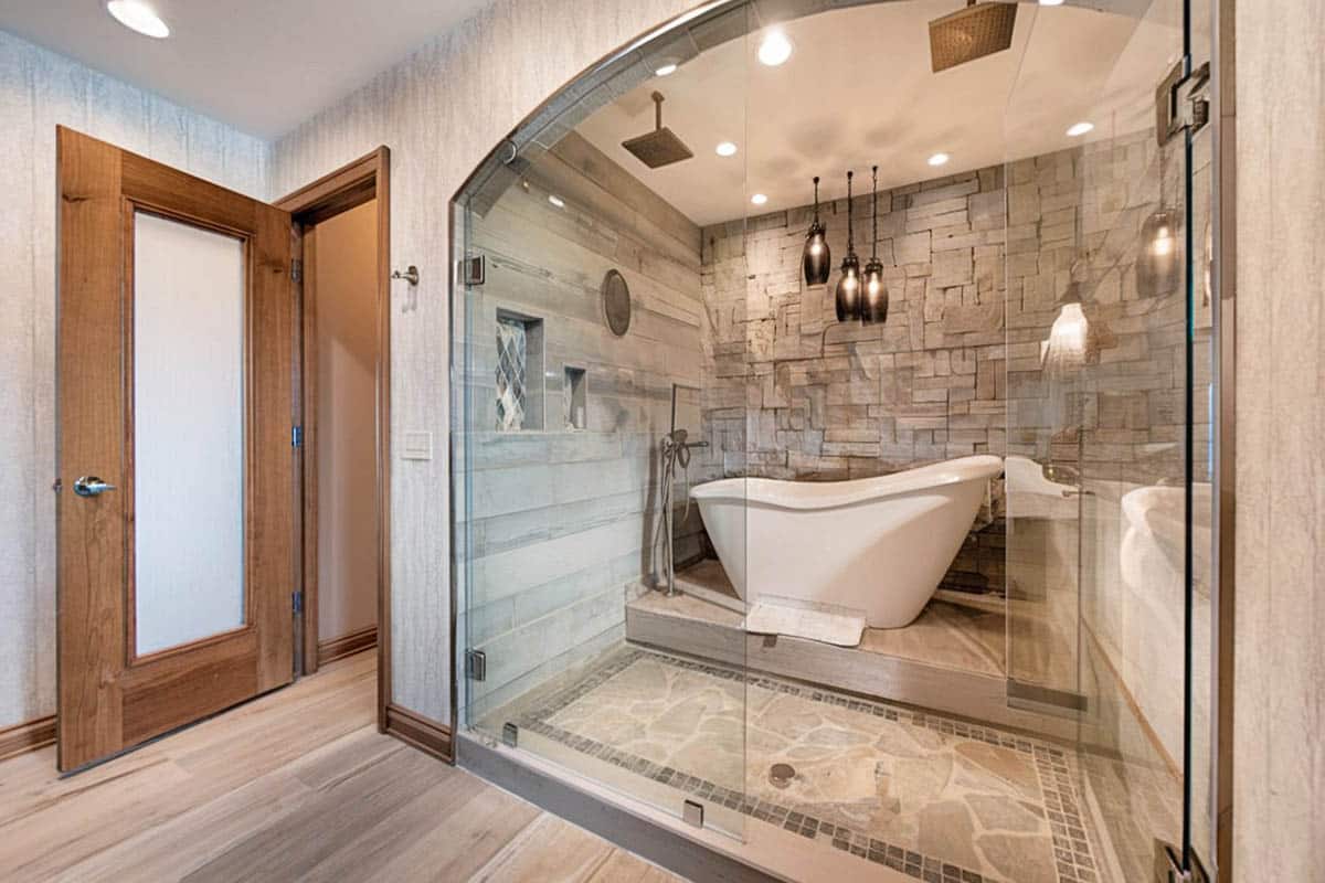Bathroom with bathtub inside on a step of the shower with stacked stone accent wall