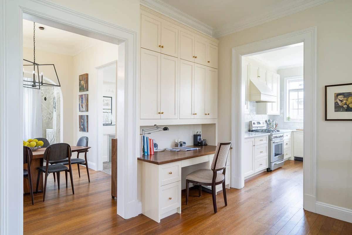 Office desk nook next to kitchen and dining room with cupboards