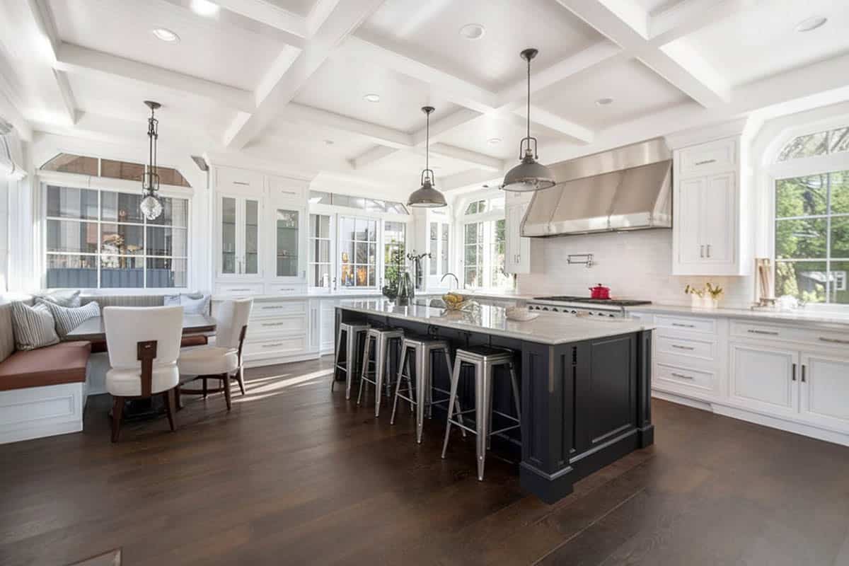 Luxury kitchen with white shaker cabinets black island dark wood flooring built in dining bench