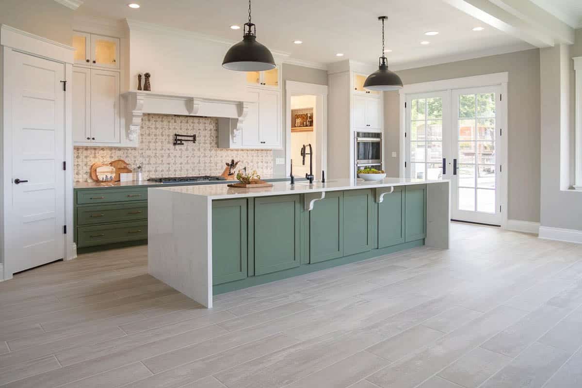 Kitchen with light hued flooring with white and green cabinets and green island