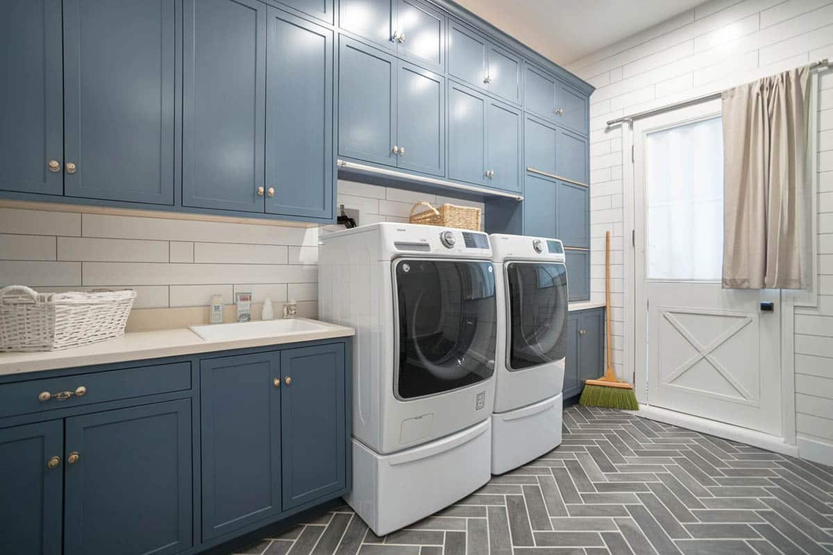 Blue painted laundry cabinets with gray herringbone tile flooring.