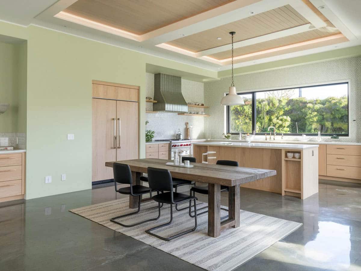 Open kitchen dining room with pale green walls, gray toned concrete surface floors and light brown cabinets