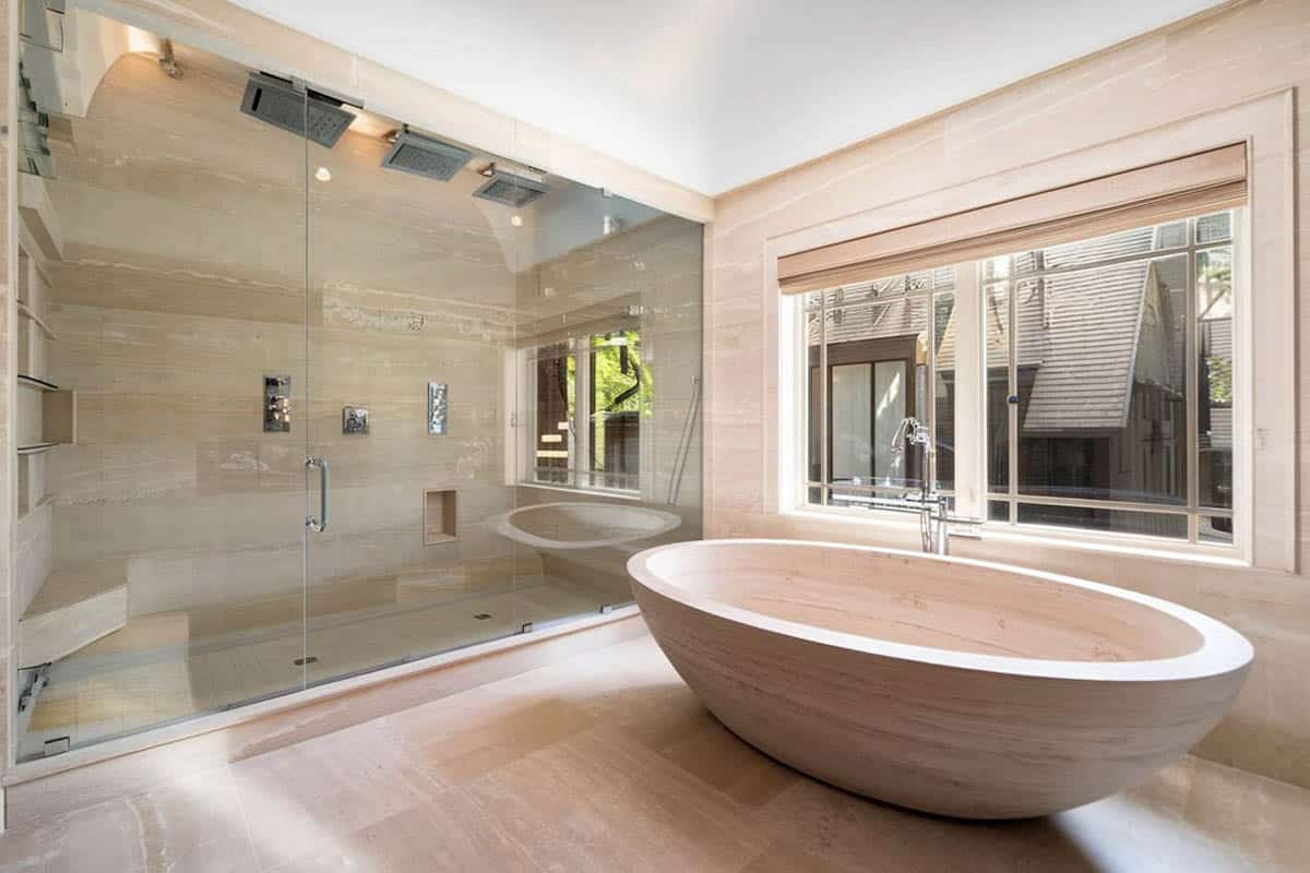 Stylish bathroom with custom travertine bathtub and large glass shower with dual rainfall showerheads