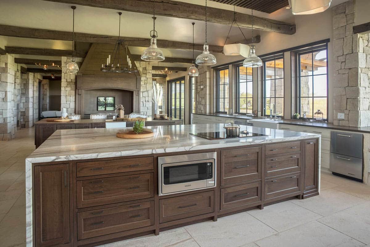 Kitchen with columns in stone cladding, beam ceiling and picture windows
