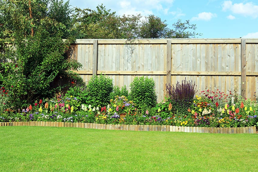 Wooden garden edging with flowering plants and large wood backyard fence