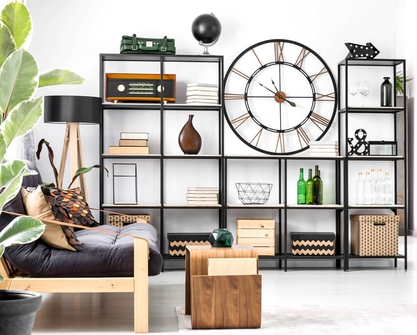 A big clock on industrial type storage rack with decorations in bright flat interior with black couch and wooden stool