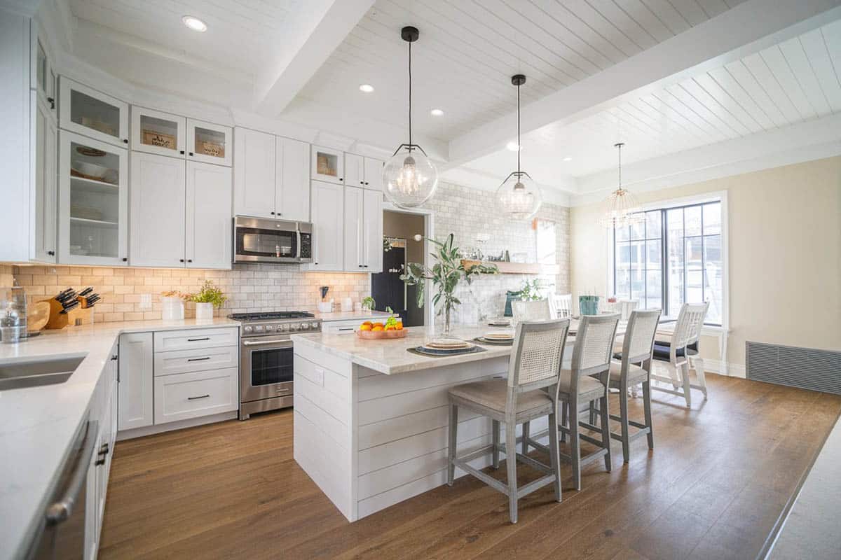 Kitchen with ceiling boards and pillar legged island, white cabinets and dark wood flooring