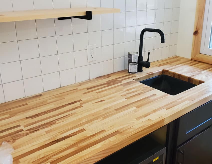 Kitchen with square tile backsplash, cedar countertop, sink, faucet, and cabinets