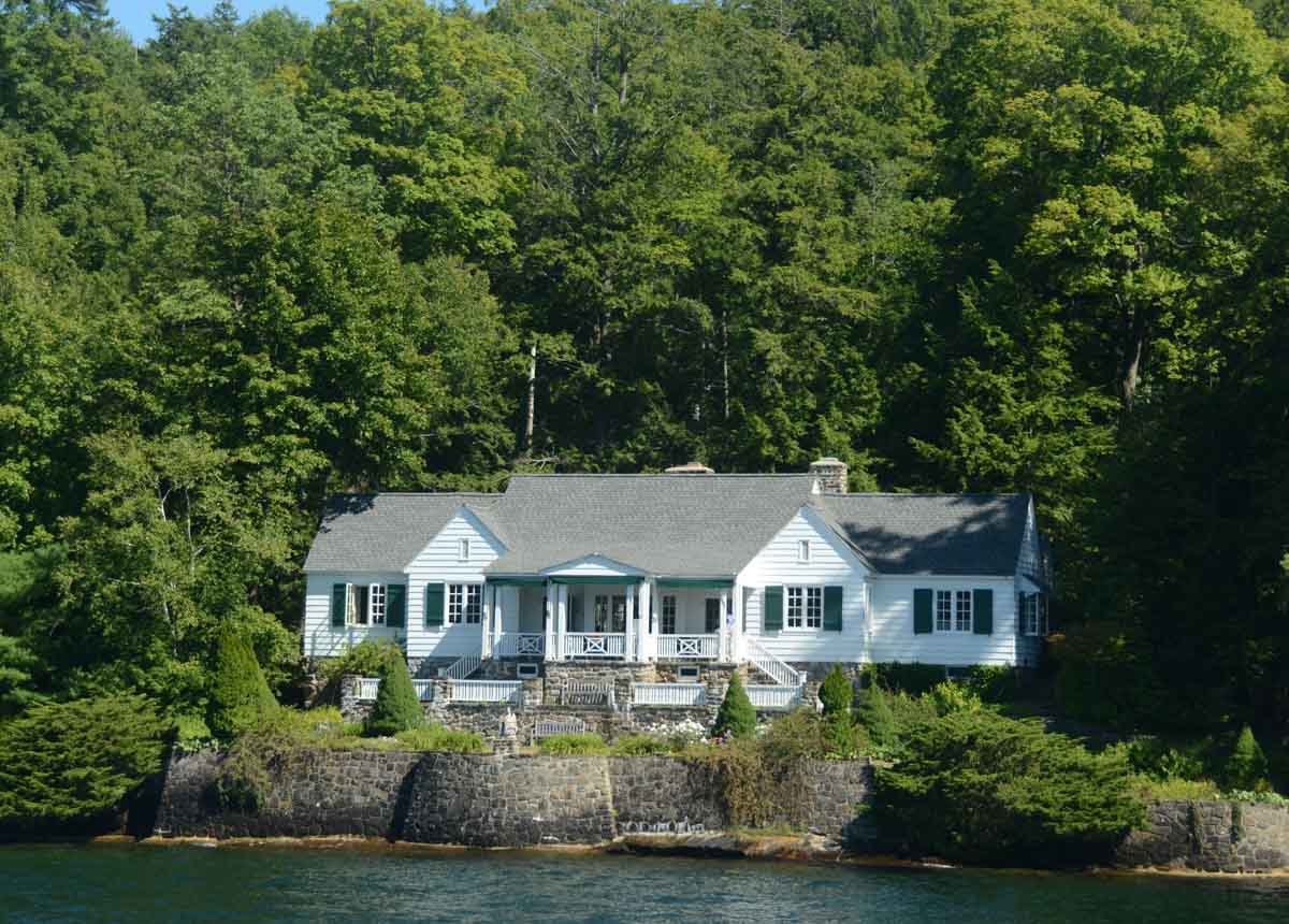 white lake home with multiple windows and shingles surrounded by trees
