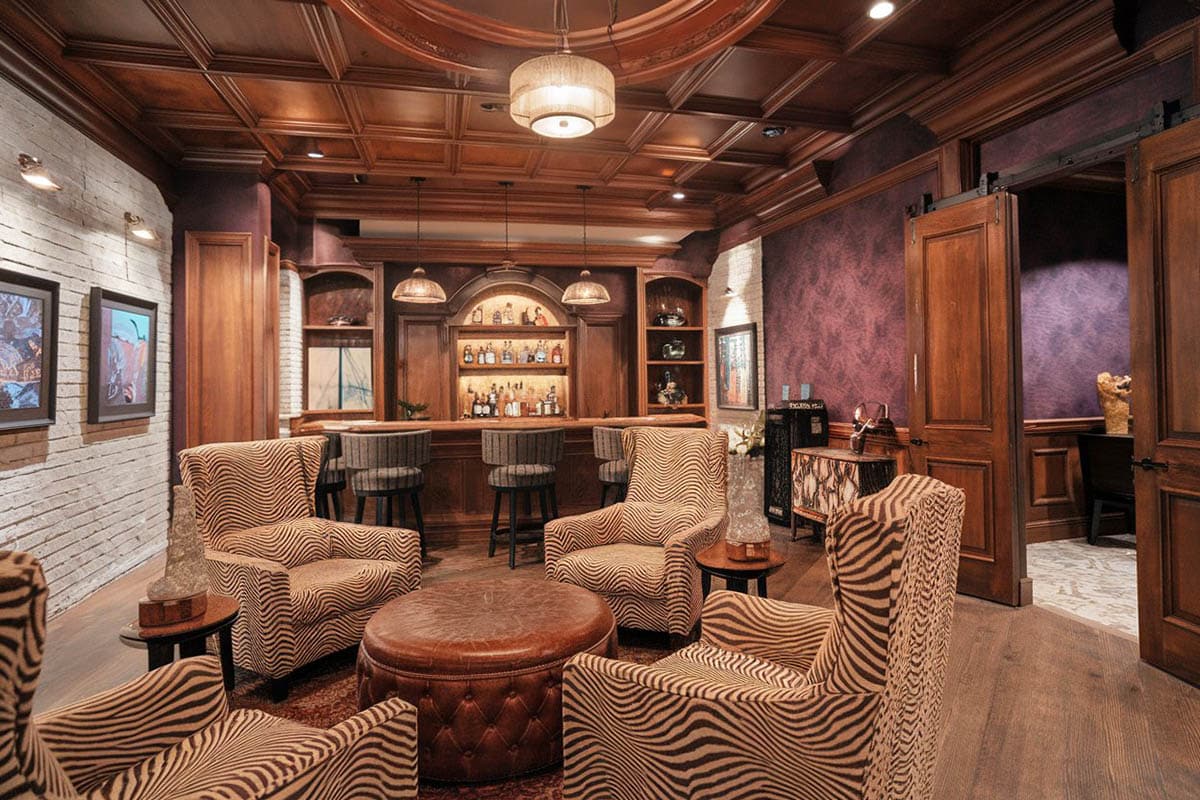 Swanky bar with patterned chairs and leather ottoman and fabric wallpaper
