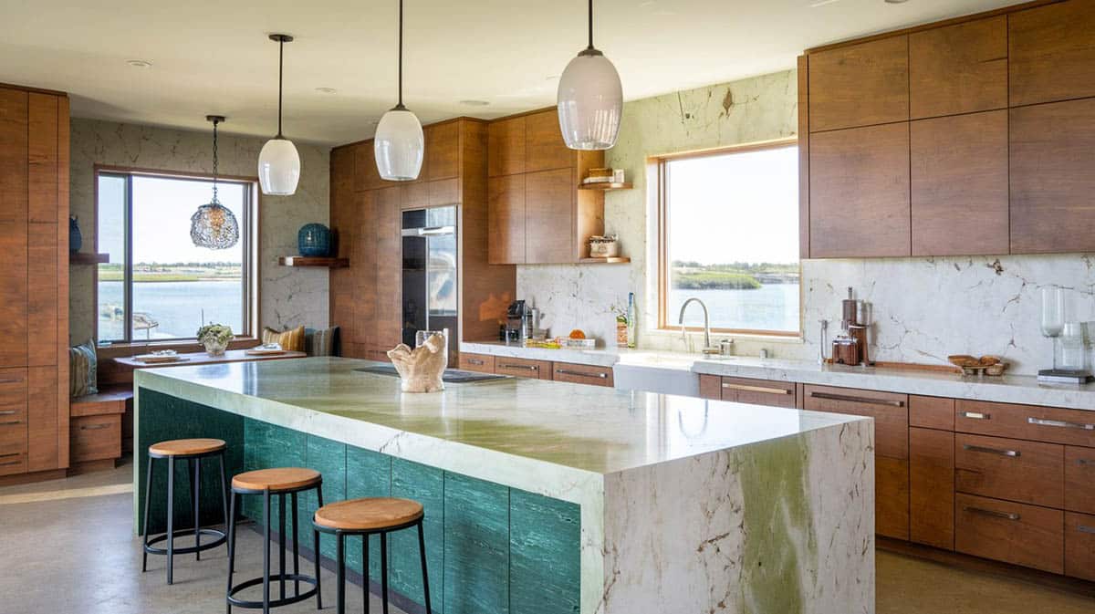Modern kitchen with a large green quartz island wood veneer cabinets and window seat views of the water